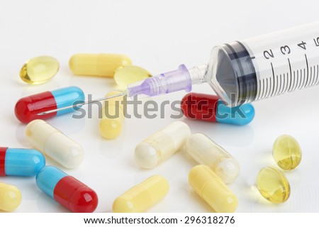 Close up of a hypodermic needle and colored capsules. Health or addiction concept.