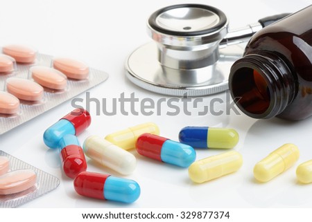 Close up of statin and beta-blocker pills and capsules with bottle and stethoscope.