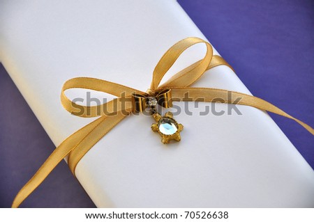 White gift box wrapped with satin golden ribbon and decorated with luxurious pin. Gift box is isolated on blue background.