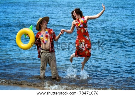 An excited couple on vacation frolic in the waves on a beach in Maui, Hawaii.