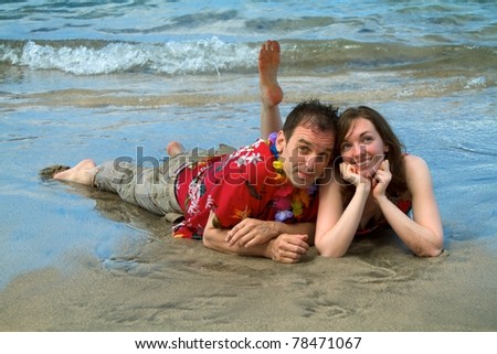 A couple vacationing in Hawaii allows the surf to wash over them as they lie on a beach in Lahaina, Maui.