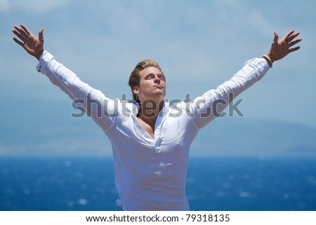 A man stands with outstretched arms on a cliffside overlooking the ocean.