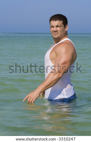 Muscular man looking into camera.  Blue sky and ocean in the background.