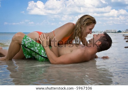 Man laying in the sand, woman laying on him, looking at each other