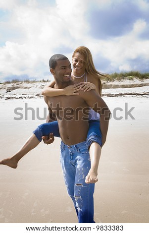 Man carrying woman on his back on a beach.