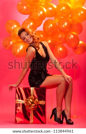 happy girl sitting on big gift box against balloons and pink background
