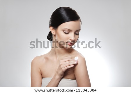 portrait of lovely girl putting cream on her shoulder over gray background