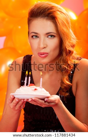 closeup portrait of lovely woman holding a birthday cake and blowing out the candles