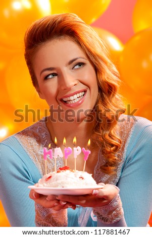 closeup portrait of happy young woman holding birthday cake with candles make a wish against balloons