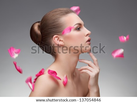 closeup portrait of beautiful young woman with flying rose petals over gray background