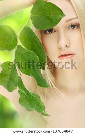 closeup portrait of lovely girl covering her face with green sprout over green background