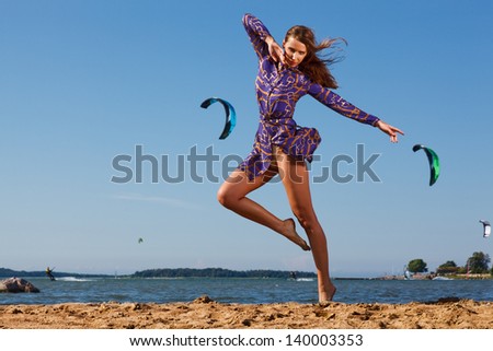 picture of beautiful young woman in dress dancing on the beach against kitesurfers