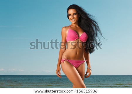 portrait of happy sexy girl in pink bikini posing against sea