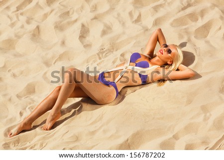 top view picture of beautiful blonde in bikini and sunglasses relaxing on the sand