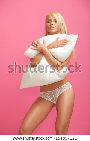 portrait of smiling sexy young woman in white lingerie with cushion posing against pink background