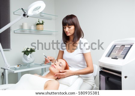 picture of pretty beautician doing microdermabrasion procedure for young woman laying down with closed eyes in a beauty salon