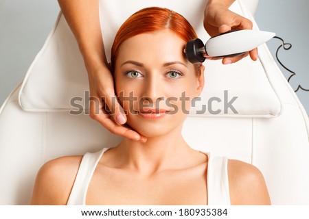 closeup portrait of happy redheaded woman getting rf-lifting in a beauty salon