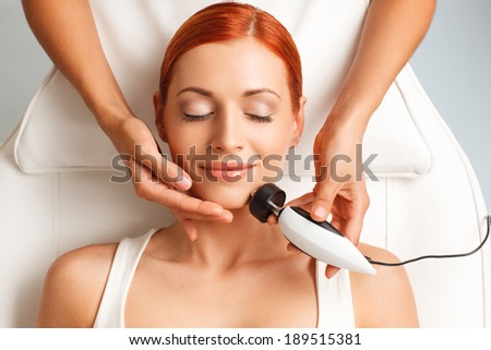 closeup portrait of happy redheaded woman with closed eyes getting rf-lifting in a beauty salon