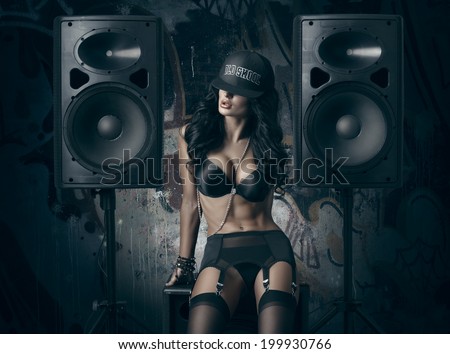 sexy girl in black lingerie and baseball cap sitting on the audio speaker against wall with graffiti