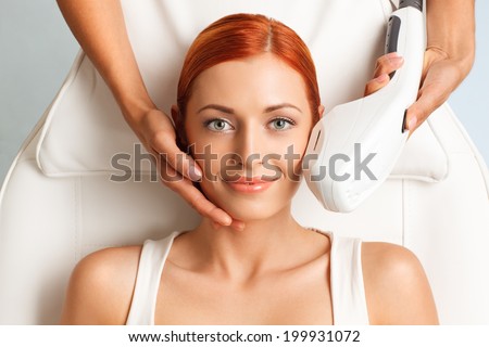 closeup portrait of happy redheaded woman getting photo rejuvenation procedure in a beauty salon