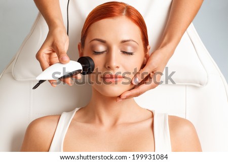 closeup portrait of lovely redheaded woman with closed eyes getting rf-lifting in a beauty salon