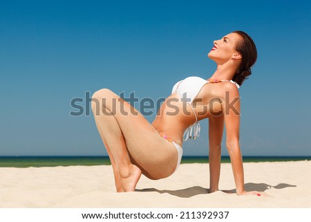 happy beautiful young woman in white bikini posing on the sand beach