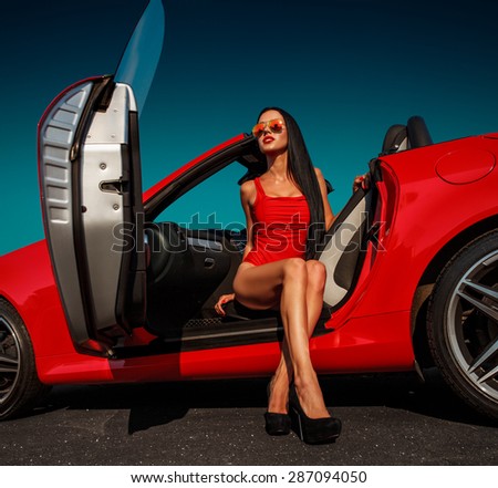 beautiful young woman with long dark hair in red bodysuit and sunglasses sitting in red cabrio