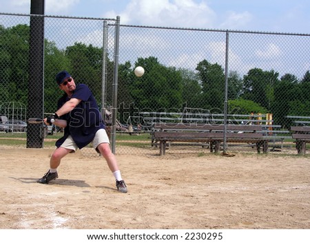 Man at a baseball diamond about to hit a softball (baseball) with ball frozen in air