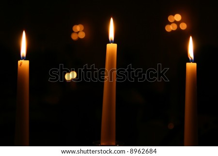 Three candles burning at night with other lights out of focus in the background