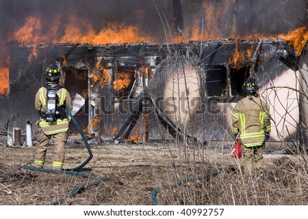 Two firefighters working to put out a fire while a home burns