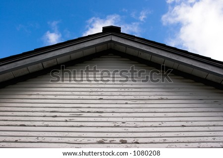 an upward view of the end of a building showing the roof and a wall with worn white paint