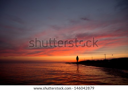 suluet lonely slim girl against the setting sun. beautiful clouds and reflections in the sea at sunset