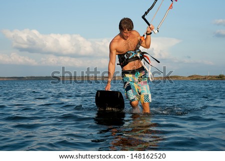 young muscular tanned kiter is reflected on the surface of the sea at sunset. tired athlete leaves the water holding a kiteboard