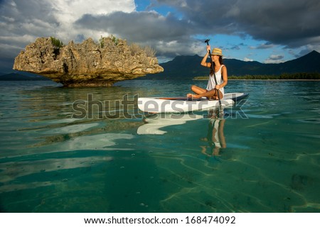 young beautiful girl-surfer riding on the stand-up paddle board in the clear waters of the Indian Ocean  of Mauritius island on the background of mountains