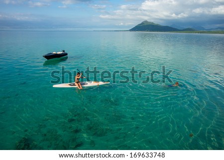 young beautiful girl-surfer riding on the stand-up paddle board in the clear waters of the Indian Ocean  of Mauritius island on the background of mountains and clouds