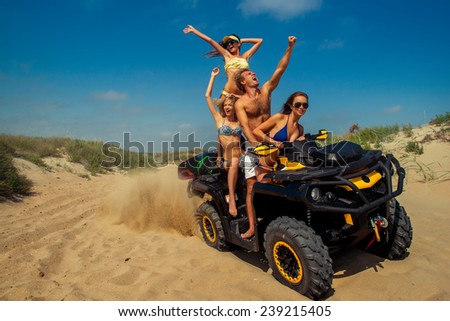 company of three beautiful girls, models, and one guy riding on ITV on the beach. They travel at high speed among the sand dunes.