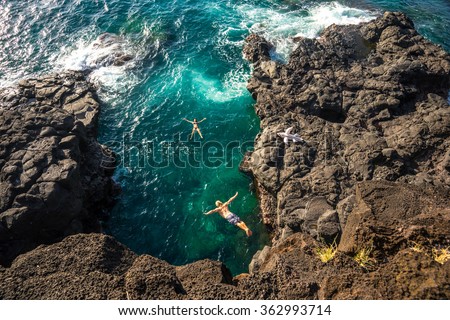 Young muscular guy jumping from a high cliff into the clear ocean on the island of Mauritius. Girl model bathes in the ocean and looking at the bottom of his jump