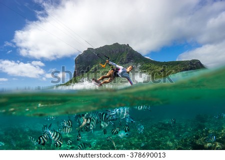 Beautiful girl with black hair kiting in the clear waters of the Indian Ocean in Mauritius with background of clouds and high mountain. The lower part of the picture - the underwater world with fishes