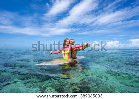 Young and beautiful couple of lovers sitting on a surfboard in the open ocean on a background of clouds. Mauritius island, Indian Ocean