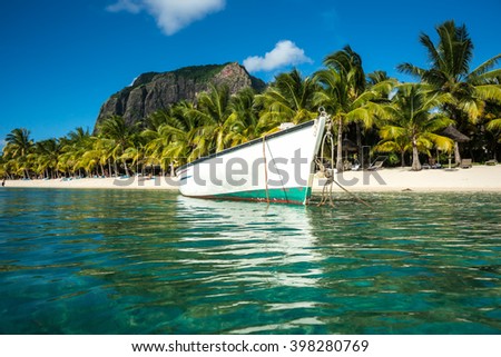 snow-white fishing boat parked in the clear emerald ocean on a background of high mountains and palm trees. Indian Ocean, Mauritius island