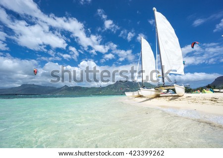 racing catamarans with white sails parked on the beach against the backdrop of the ocean, clouds, mountains and kites. Mauritius, Indian Ocean