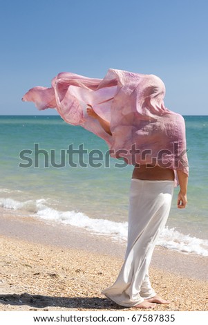 Tanned girl in a pink headscarf and a white skirt against the bright blue sky and turquoise sea