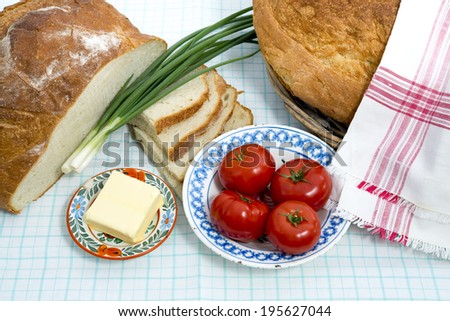 Fresh bread and butter with tomatoes and fresh onion on a table cloth/  Picnic country side lunch / Fresh round bread with slices, butter and vegetables on a table