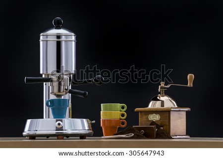 Vintage espresso machine with cups and grinder on black background / Old espresso maker on a table / Vintage coffee maker on black background