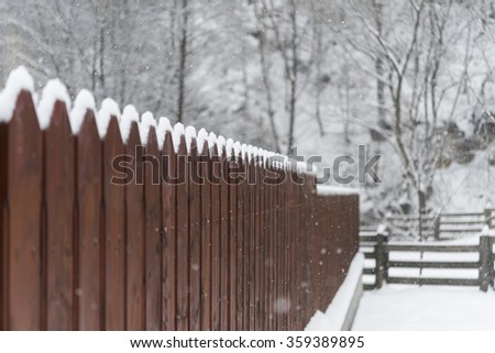 Brown garden fence with snow / Snowing on house wooden fence / Backyard brown wood fence covered in snow