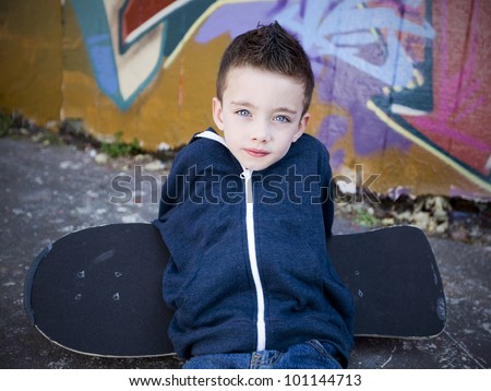 Young boy with skateboard against a graffiti wall