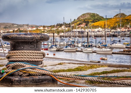 Close up view of harbor bollard with mooring ropes and colorful cables wrapped around it. A Scenic view of North Wales with sailing boats and  the Welsh hills in the distance.