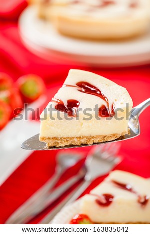 Strawberry Cheesecake slice sitting on cake knife with strawberries and red background. Vertical composition.