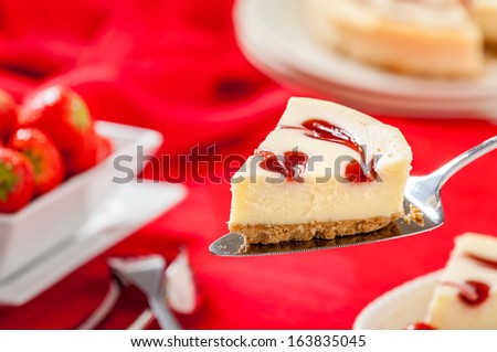 Strawberry Cheesecake slice sitting on cake knife with strawberries and red background. Horizontal composition.