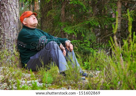 Old man resting in a forest near a tree